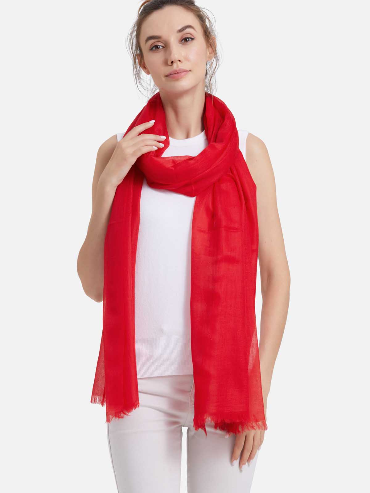 A woman modeling a lightweight, featherlight cashmere scarf with fringed edges, styled over a white sleeveless top and white pants against a plain light gray studio background.
