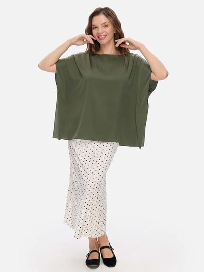 Woman wearing a green silk top and white polka dot skirt on a white background