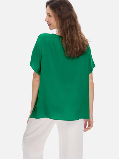 Woman wearing a green silk top and white pants on a light gray background