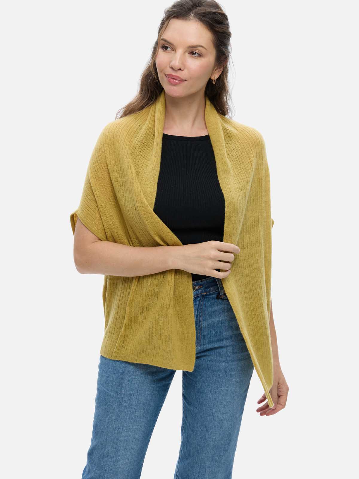 Woman wearing a mustard yellow cashmere vest over a black top and blue jeans on a white background