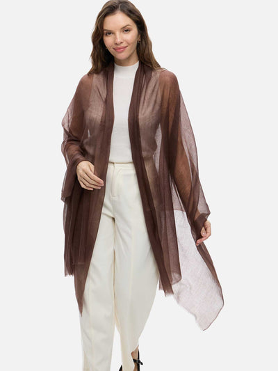 A woman modeling a sheer, lightweight featherlight brown cashmere scarf over a white top and white pants, set against a plain light gray studio background.
