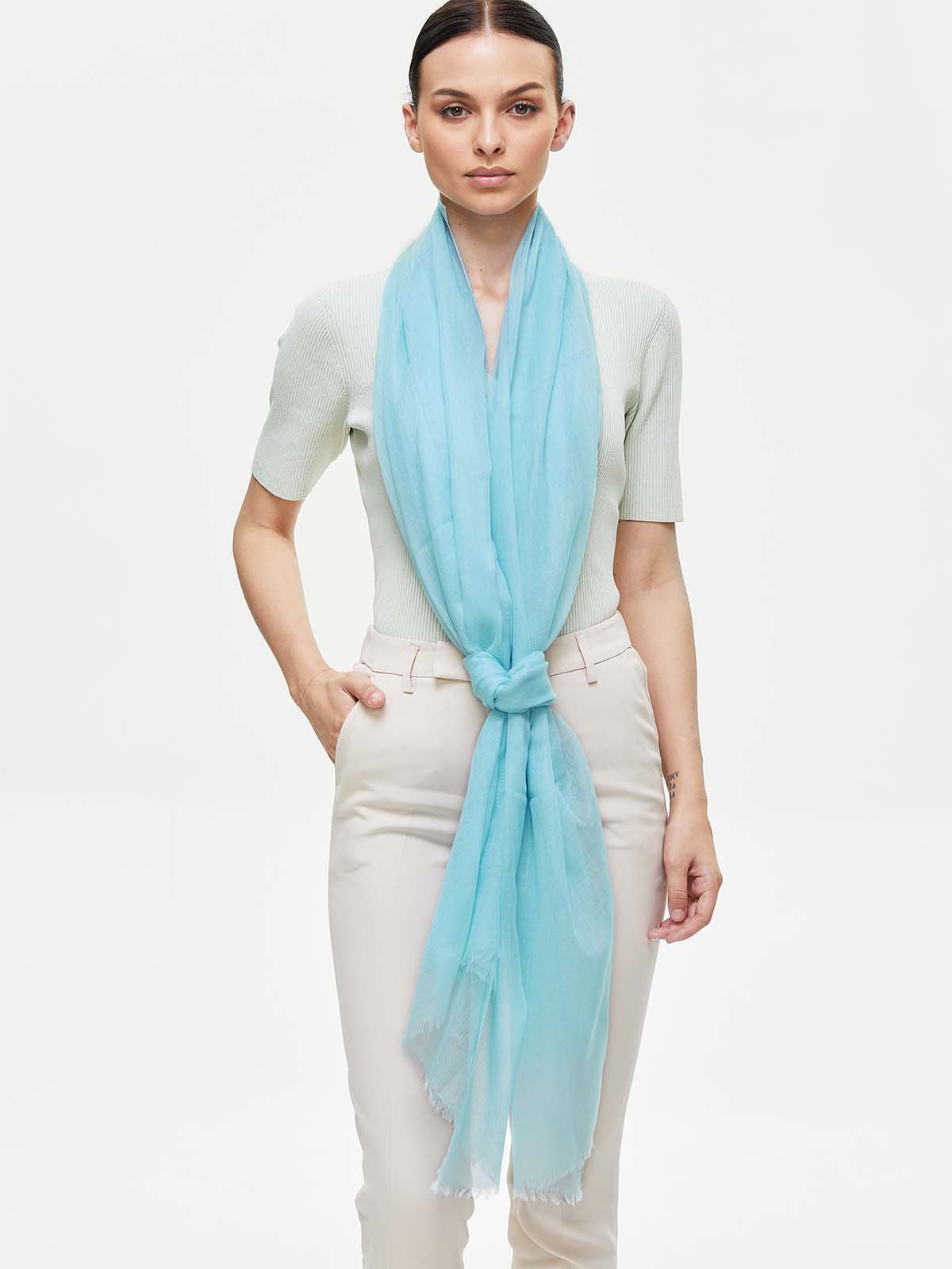 Woman wearing a featherlight light blue cashmere scarf on a white background