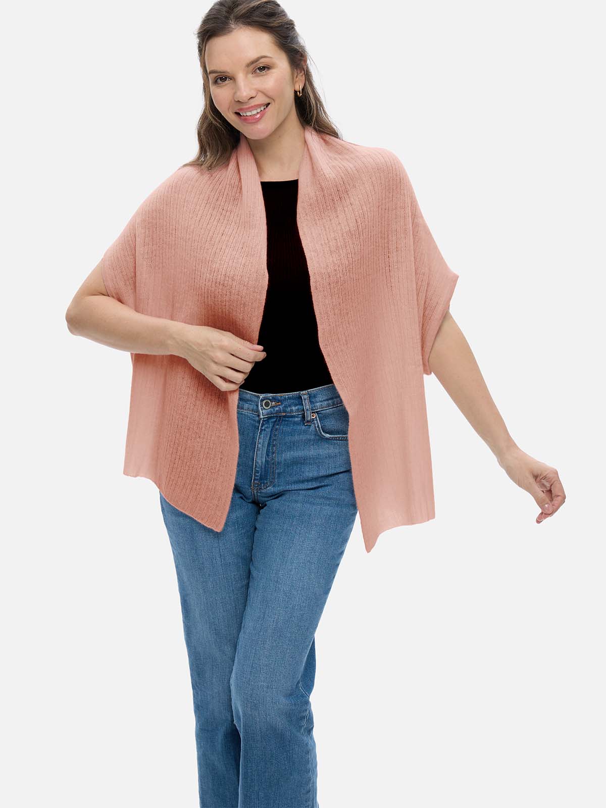Woman wearing a pink cashmere vest over a black top and blue jeans on a white background