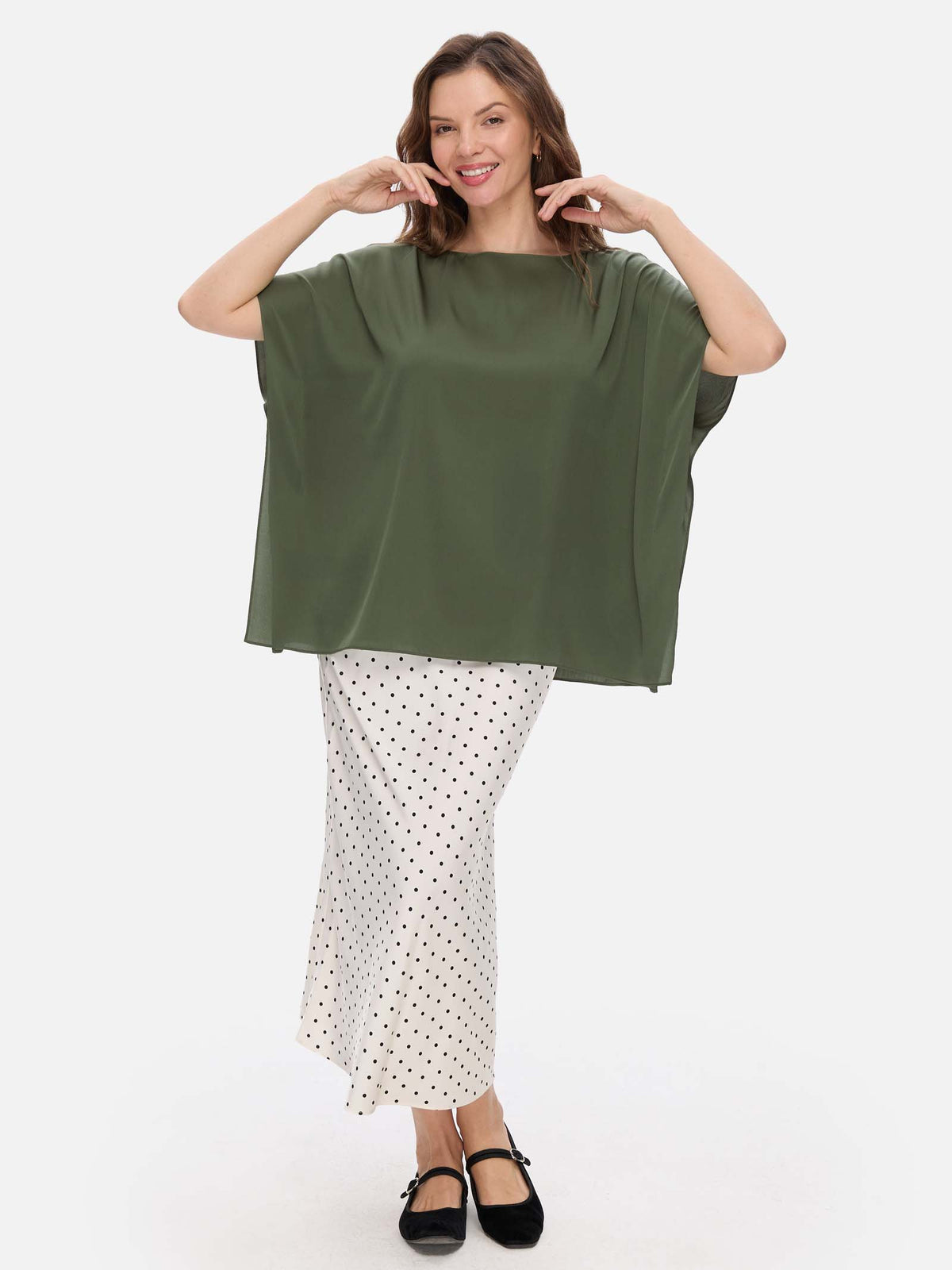 Woman wearing a green oversized silk top and white polka dot skirt on a white background