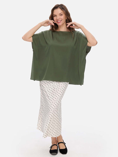 Woman wearing a green oversized silk top and white polka dot skirt on a white background
