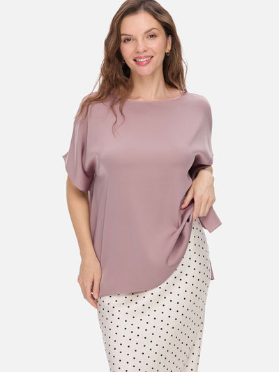 Woman wearing a mauve silk top and polka dot pants on a white background