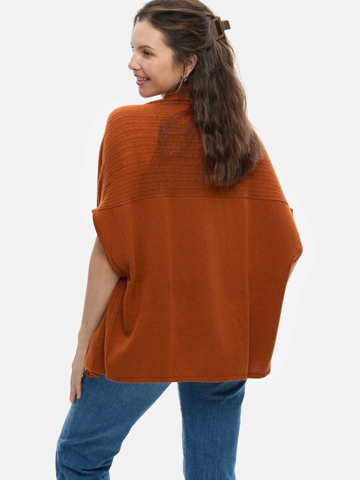 Woman wearing a rust-colored cashmere vest over a blue top on a white background