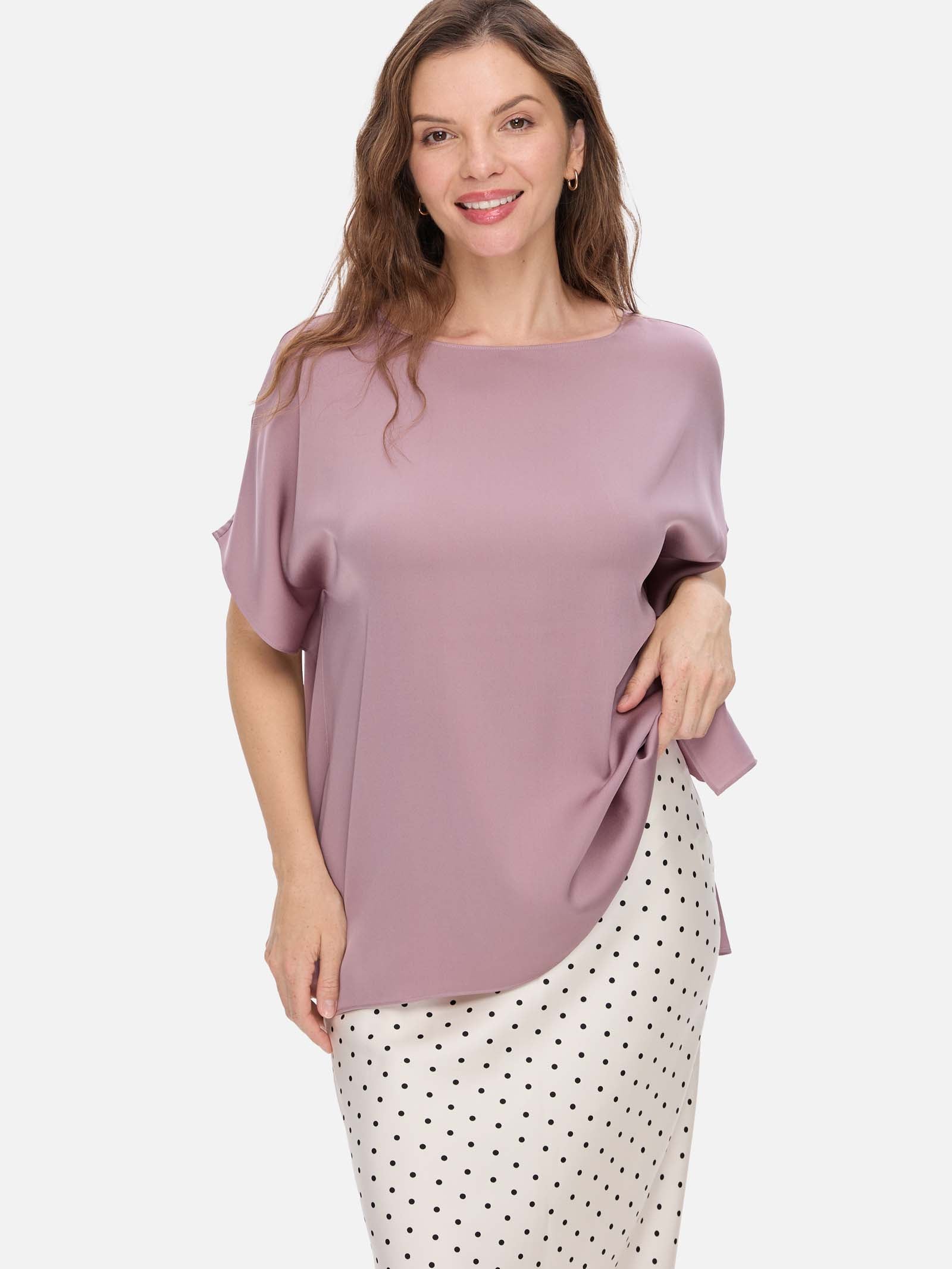 Woman wearing a mauve silk top and polka dot pants on a white background