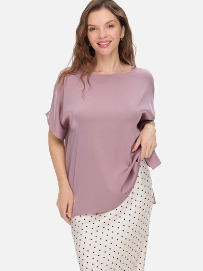 Woman wearing a mauve silk top and polka dot pants on a white background