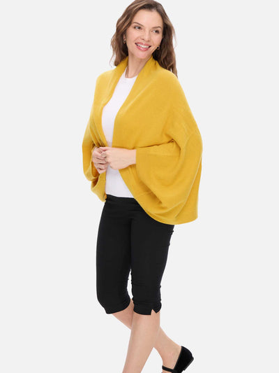 Woman wearing a mustard yellow cashmere wrap over a white shirt and black pants on a white background