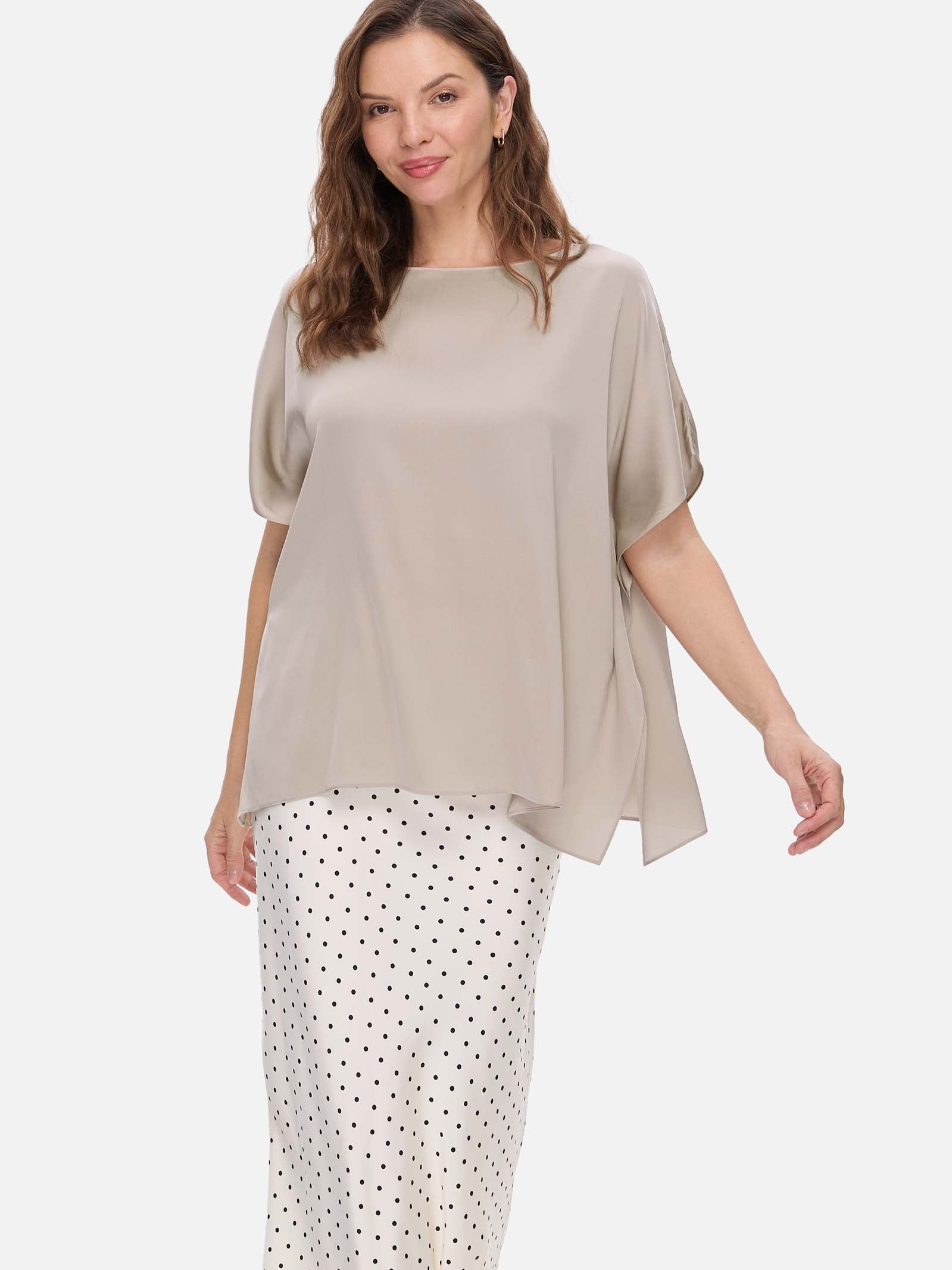 Woman wearing a beige silk top and polka dot pants on a white background