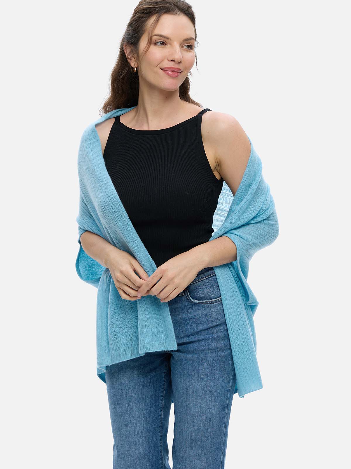 Woman wearing a light blue cashmere vest over a black top and jeans on a white background