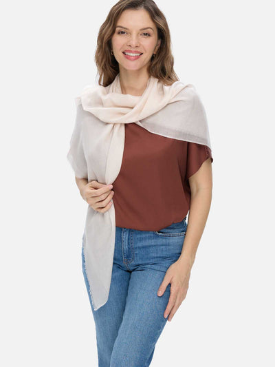 Woman wearing an ivory Square Featherlight Cashmere Scarf draped over her shoulders, styled with a rust-brown top and blue jeans.