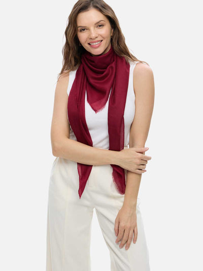 Woman wearing a wine red Ovcio Featherlight Cashmere Scarf over a white top and ivory trousers.