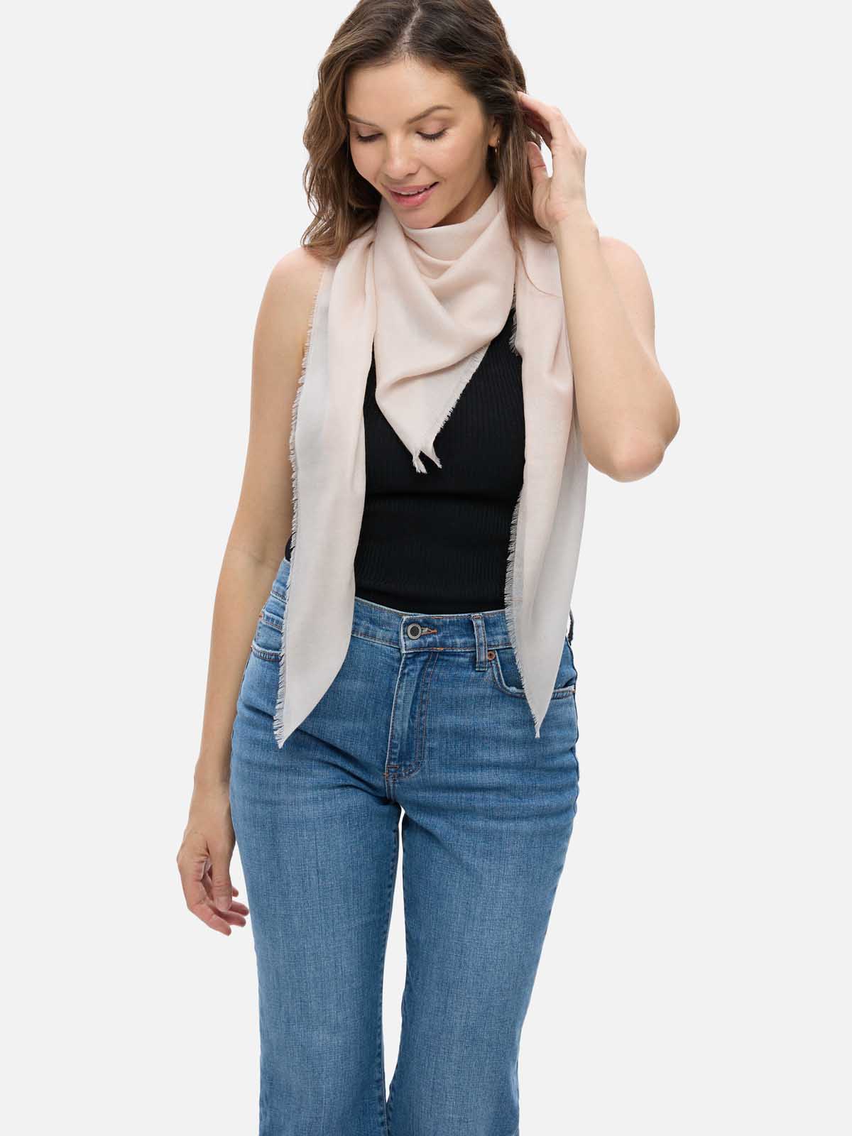 Woman wearing an Ivory Square Featherlight Cashmere Scarf draped over her shoulders, styled with a black top and blue jeans.