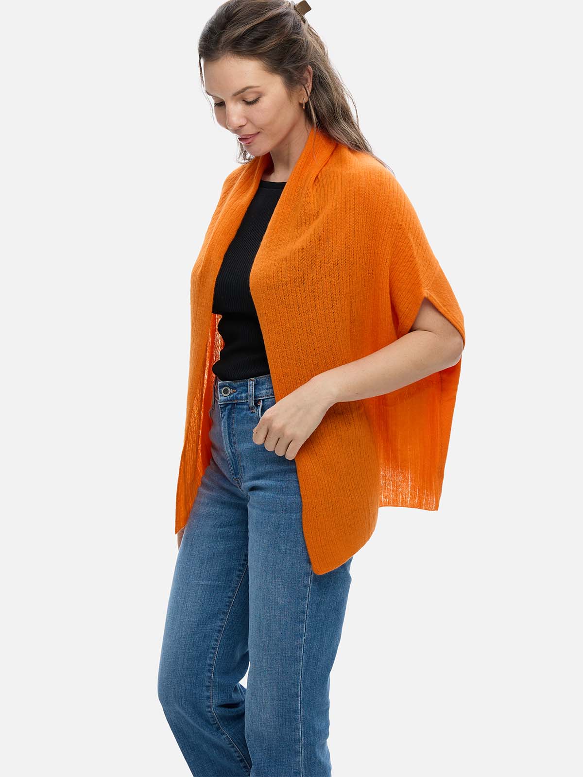 Woman wearing an orange cashmere vest over a black top and blue jeans on a white background