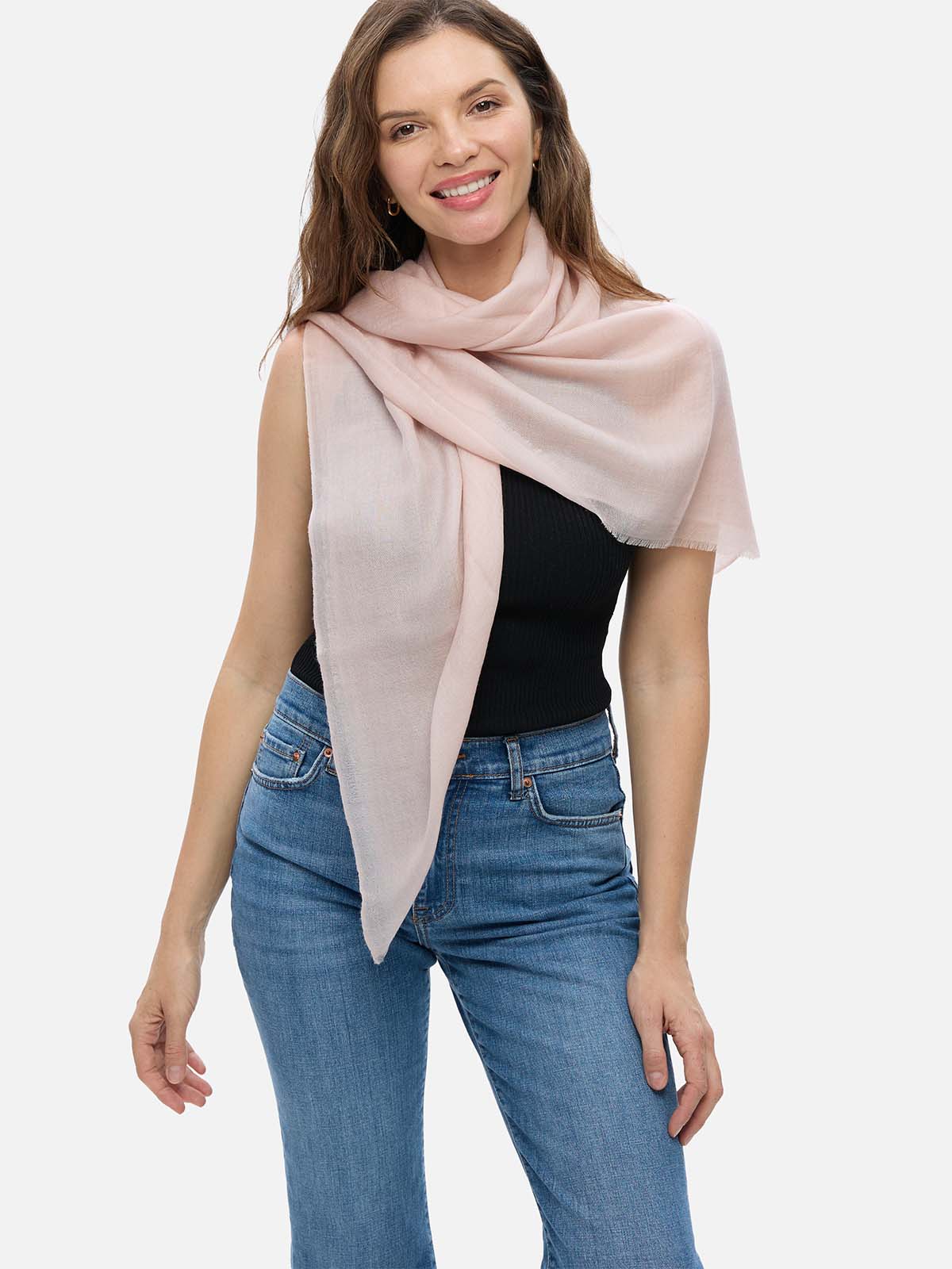 Woman wearing a blush Square Featherlight Cashmere Scarf wrapped around her neck and shoulders with a black sleeveless top and blue jeans.