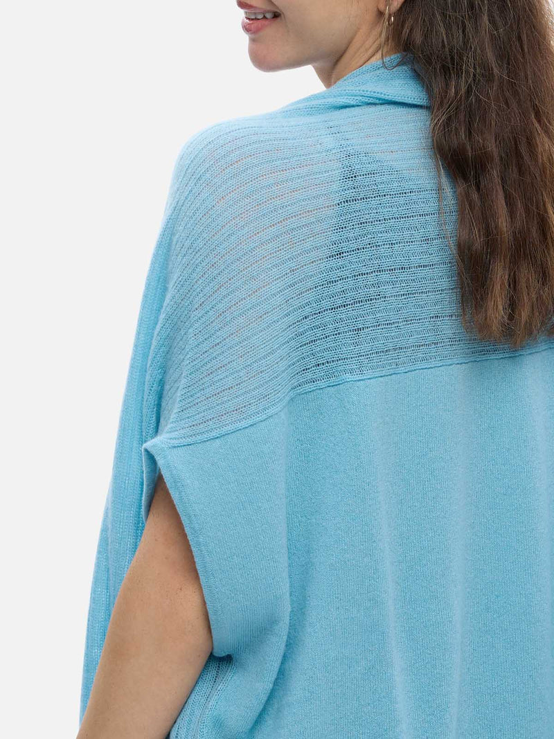 Woman wearing a light blue cashmere vest over a black top and jeans on a white background