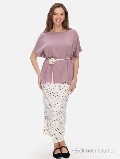 A woman modeling a mauve short-sleeve silk top with a white belt featuring a large flower detail, paired with a white and black polka dot skirt, against a light gray background. Text at the bottom right reads 'Belt not included'.
