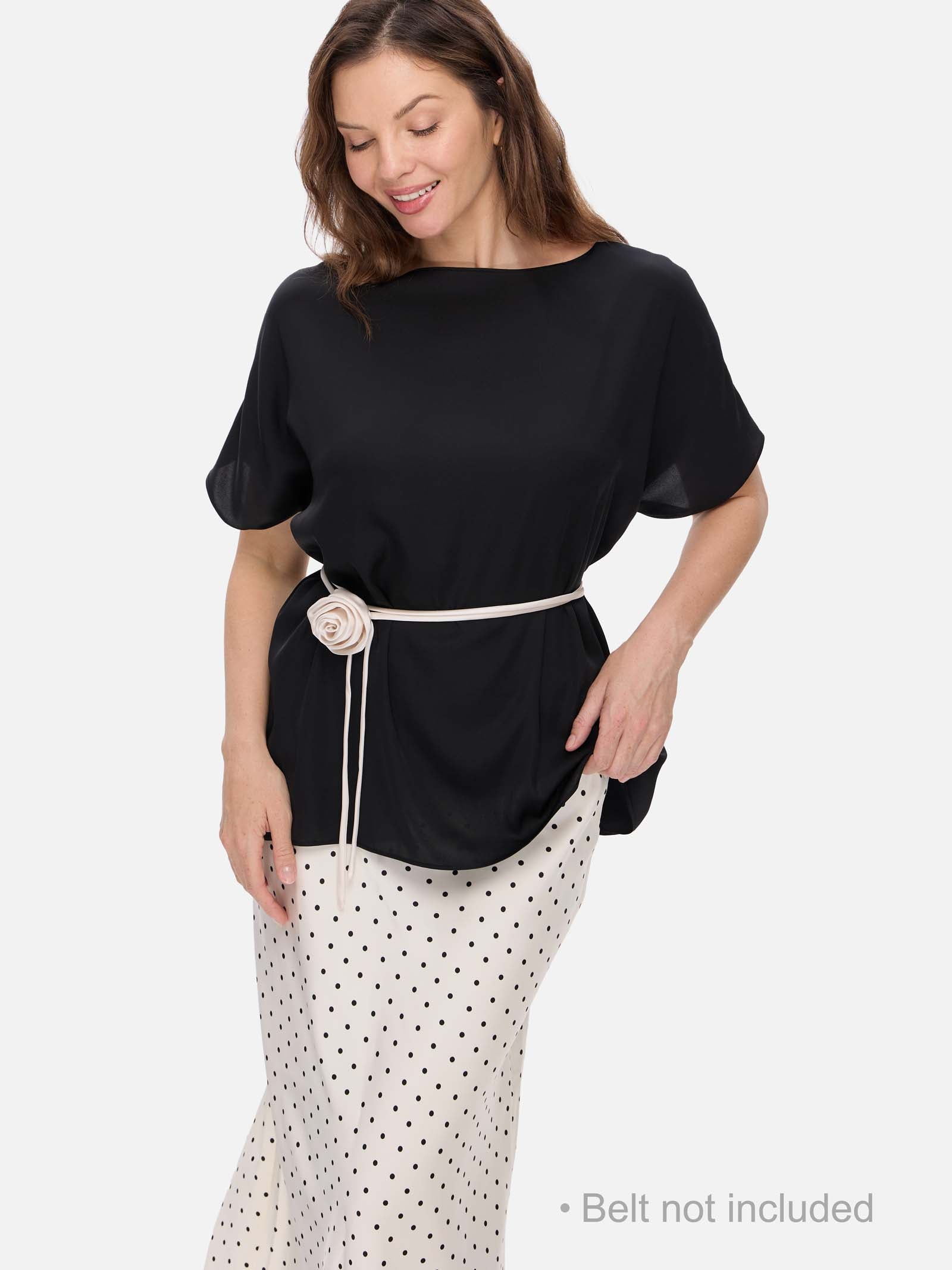 Woman wearing a black silk top and white polka dot pants on a light gray background
