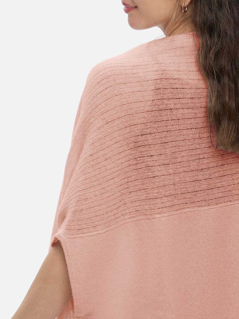 Woman wearing a pink knitted cashmere vest over a black top and blue jeans on a white background