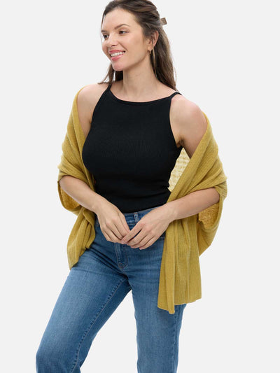 Woman wearing a mustard yellow cashmere vest over a black tank top and blue jeans on a white background