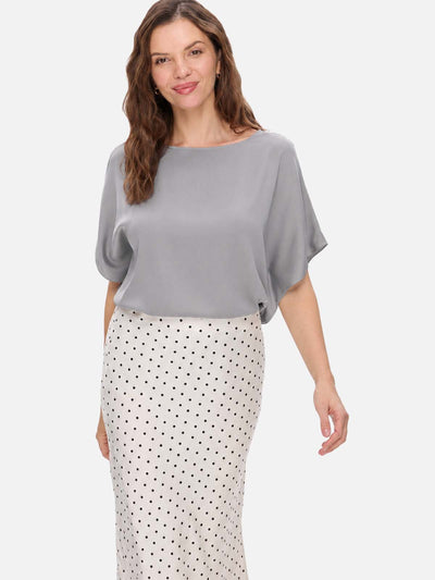 A woman modeling a light gray short-sleeve silk top with a boat neckline and a white skirt with black polka dots, set against a plain light gray background.