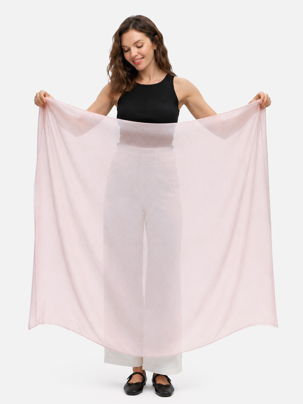 A woman modeling a large, lightweight, semi-sheer featherlight blush cashmere scarf, holding it wide open against a plain white studio background.