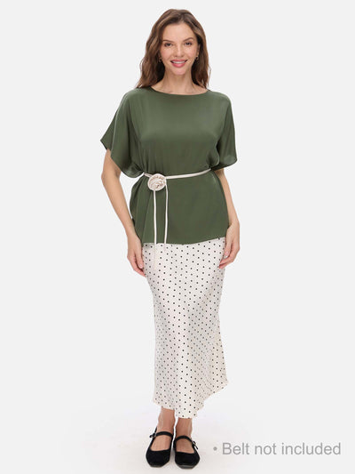 Woman wearing a green silk top and white polka dot skirt on a white background