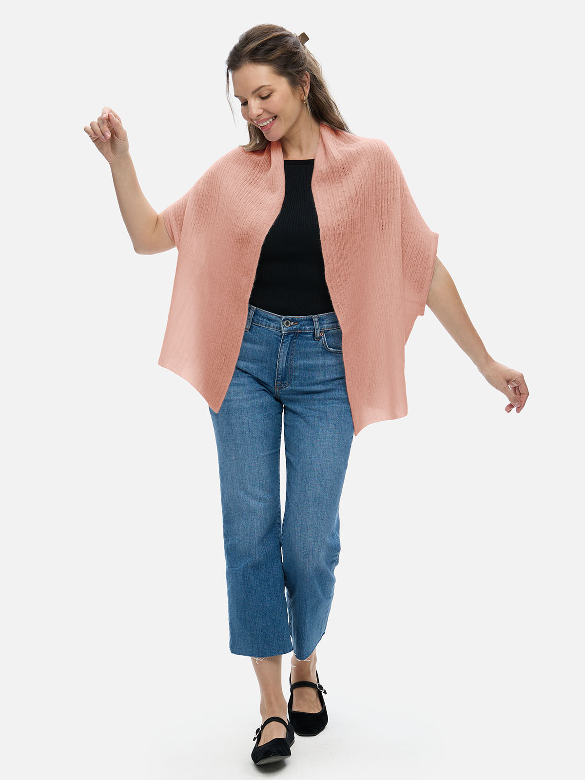 Woman wearing a pink cashmere vest, black top, and blue jeans on a white background