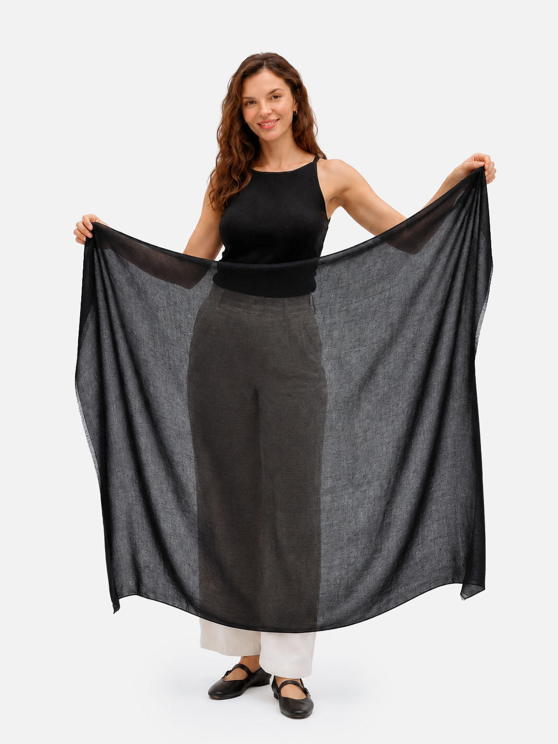 A woman modeling a large, semi-sheer black cashmere scarf, holding it out wide to show its drape and texture against a clean white background.