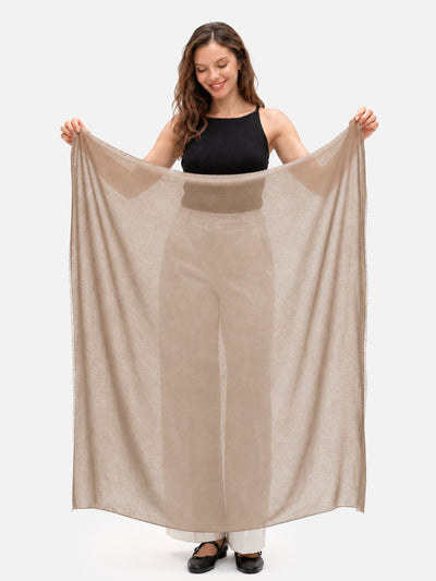 A woman holds up a large, semi-sheer Camel Featherlight Square Cashmere Scarf against a plain white studio background.