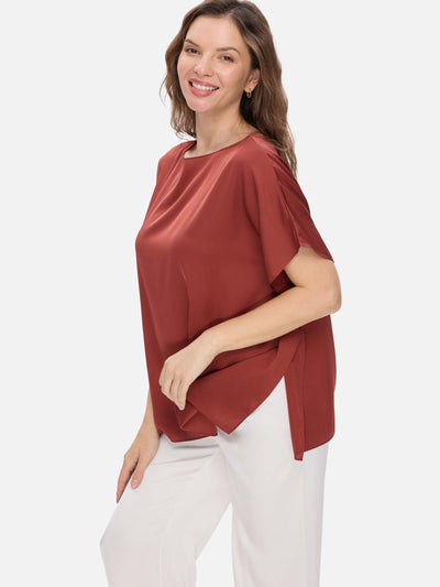 Woman wearing a rust-colored silk top and white pants on a white background