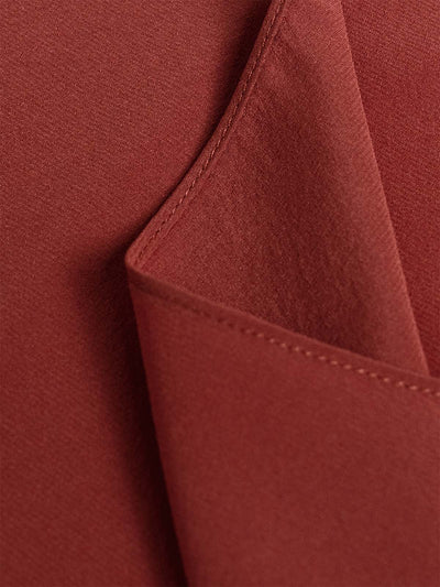 Close-up of a rust red or terracotta-colored silk fabric with a folded corner showing fine texture and matching stitching.