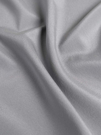 A close-up of draped light gray silk fabric with soft folds and a smooth texture.