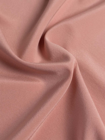 A close-up of draped dusty pink silk fabric with soft folds and a smooth texture.