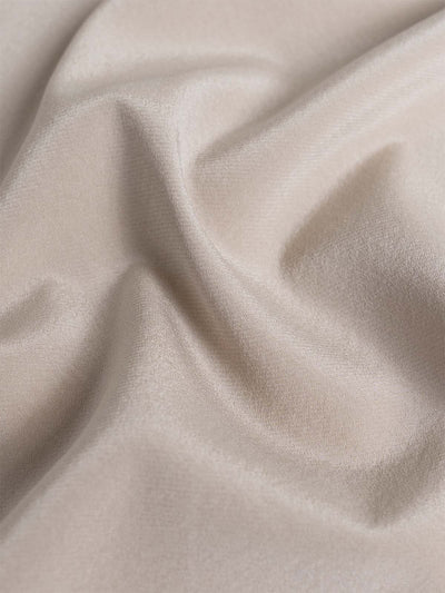 A close-up of draped silk fabric in a light cream or ivory color, showing soft folds and a subtle sheen.