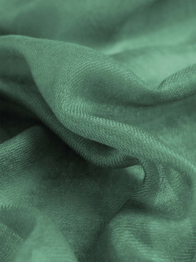 A close-up of draped sage green cashmere scarf with a soft, textured weave and gentle folds.